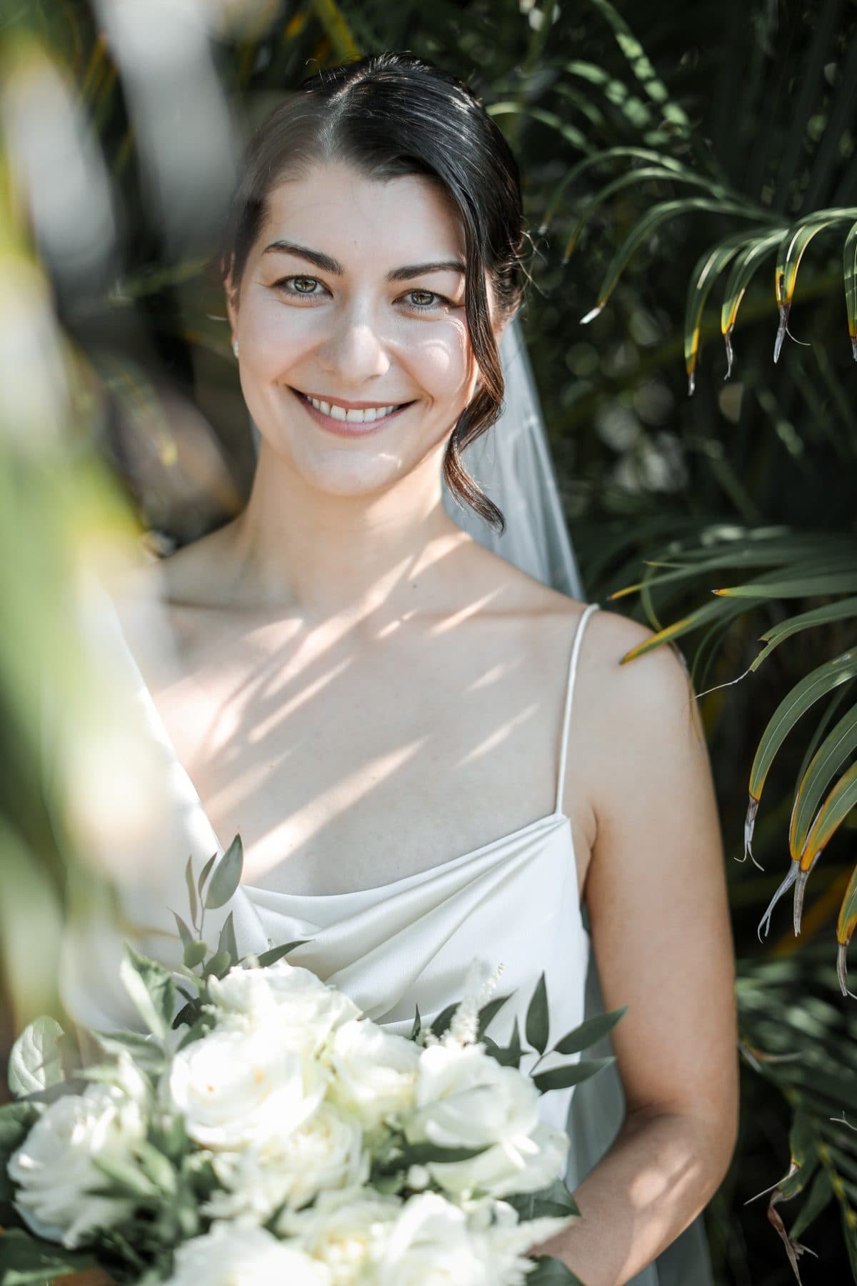 A smiling bride with a white rose bouquet in a tropical garden in Okinawa